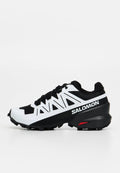 Schwarz-weißer Salomon Trailrunning-Schuh mit aggressivem Profil, schwarzen Schnürsenkeln und weißen geometrischen Überzügen an den Seiten.