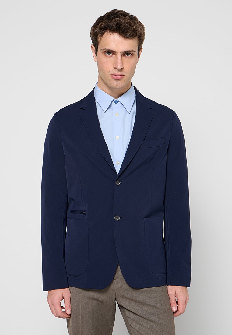 Marineblazer aus glattem Stoff mit einem einzelnen Knopfverschluss, zwei Vorderentaschen und einem Revers mit Kerbkragen. Wird über einem hellblauen Hemd getragen.