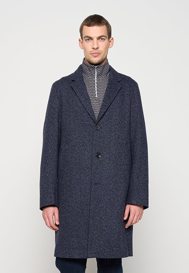 Marineblauer Wollmantel mit Struktur, ausgeführt mit Reverskragen, Einzelknopfverschluss und zwei Fronttaschen, kombiniert mit einem gemusterten, Reißverschluss-Pullover.