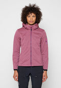 Frau mit rosa Softshelljacke mit Reißverschluss und Kapuze sowie schwarzen Cargohosen steht vor einem schlichten hellen Hintergrund.
