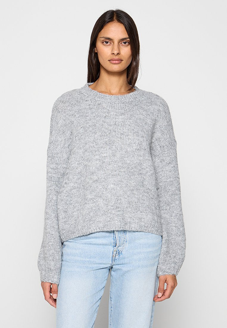 Grauer Strickpullover mit rundem Ausschnitt, überschnittenen Schultern und langen Ärmeln. Der Stoff hat eine weiche, strukturierte Oberfläche.