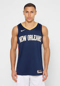 Junger Mann, der nach vorne blickt, trägt ein dunkelblaues New Orleans Basketball-Trikot und weiße Shorts vor einem schlichten Hintergrund.