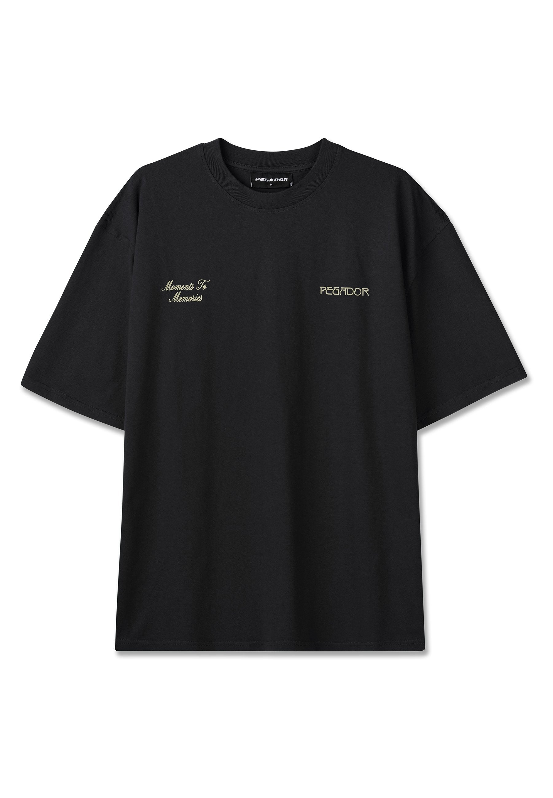 Schwarzes T-Shirt mit kurzen Ärmeln, links auf der Brust mit dem Schriftzug „Moments To Memories“ und rechts auf der Brust mit „PEGADOR“ in hellbeiger Schrift.