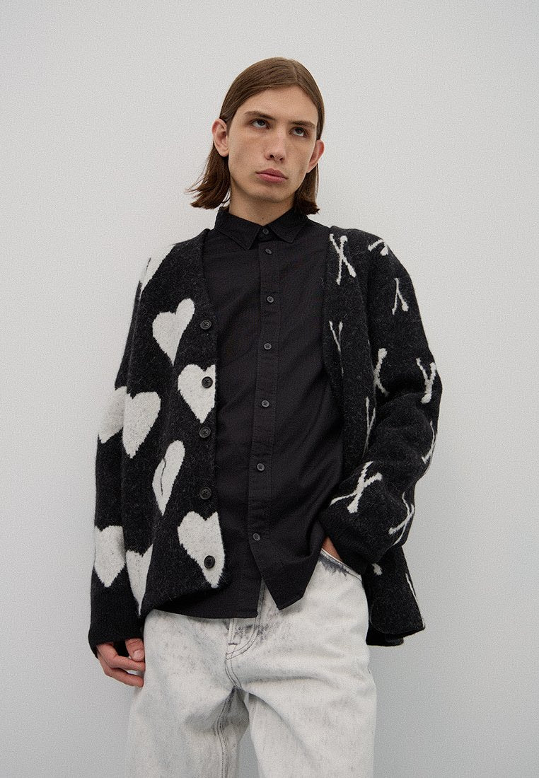 Schwarz-weiße Strickjacke mit Herz- und Knochenmustern, oversize Passform mit Knöpfen, über einem schwarzen Hemd mit Knöpfen und hellblauen Jeans getragen.