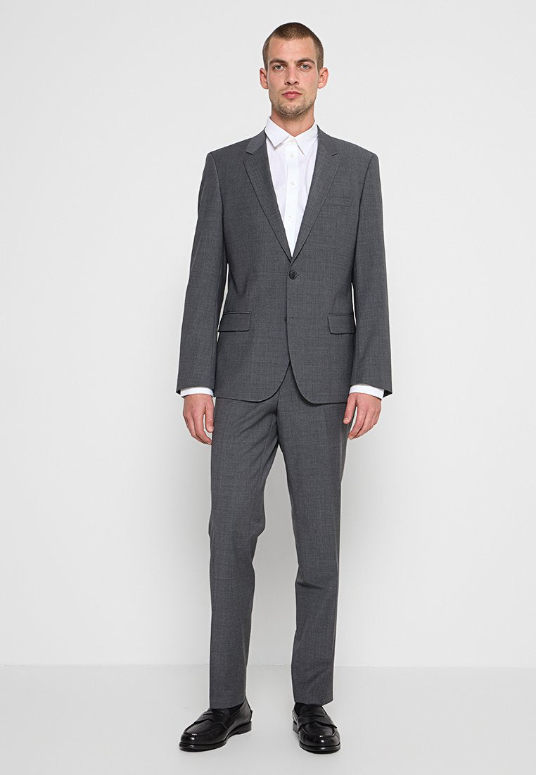 Grauer, maßgeschneiderter Anzug mit schmaler Passform, Ein-Knopf-Blazer und flachen Vorderhosen. Darunter ist ein knitterfreies weißes Hemd sichtbar. Polierte schwarze Schuhe.