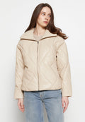 Beige Kunstlederjacke mit diamantförmigem Steppmuster, hohem Kragen, Frontreißverschluss und lockerer Passform, kombiniert mit hellblauen Jeans.