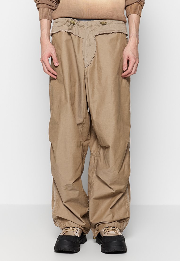 Beige, lockere Hose aus einem strukturierten, leichten Material. Verfügt über einen verstellbaren Bund und fransige Details an den Taschen.