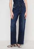 Weite Jeans aus dunkelblauem Denim mit fünf Taschen, Knopfschluss und goldenen Nähten. Kombiniert mit gemusterten Slippern.