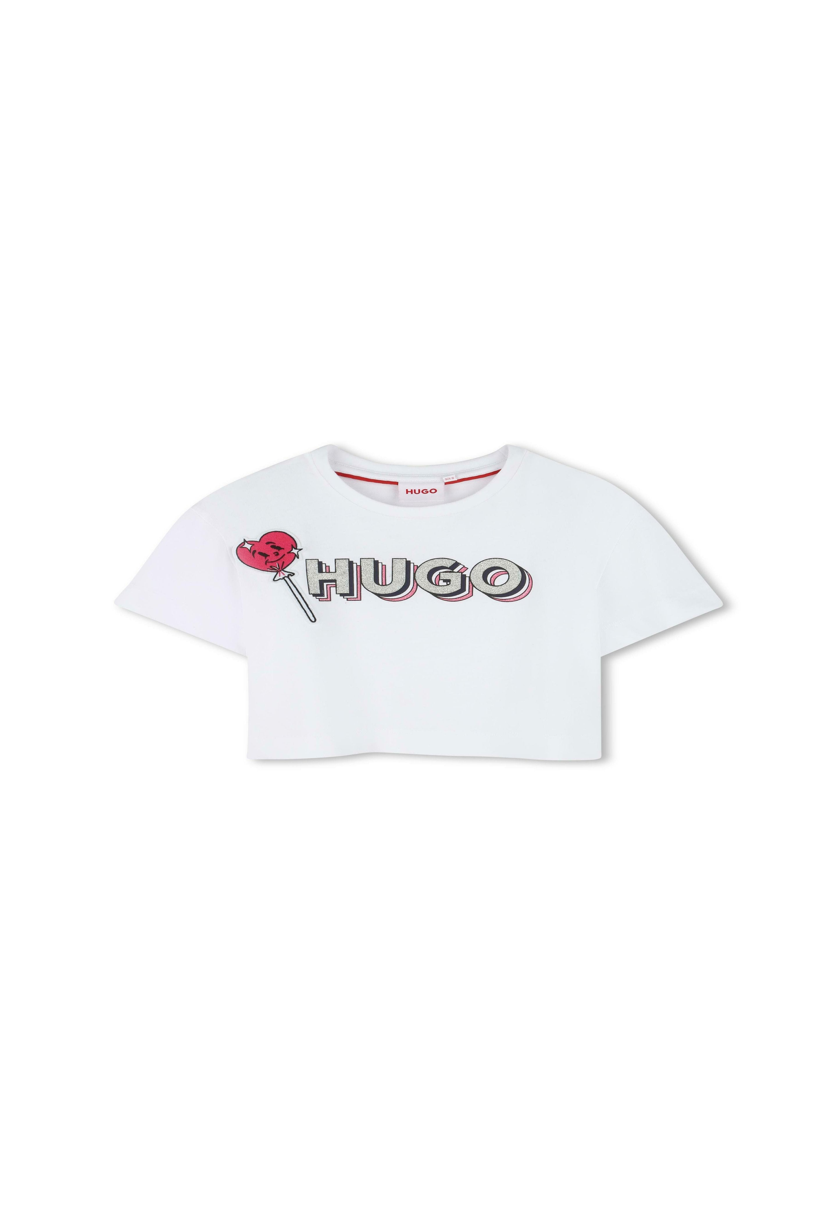 Weißes, kurzes T-Shirt mit dem Aufdruck "HUGO" in fetten Buchstaben, begleitet von einer roten Lutschersgrafik. Kurze Ärmel und runder Halsausschnitt. Glatte Textur.