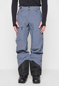 Blaugraue Skihose mit schwarzen verstärkten Unterschenkeln, Reißverschlusstaschen, verstellbarem Bund, getragen mit schwarzen Stiefeln und einem schwarzen Langarmoberteil.