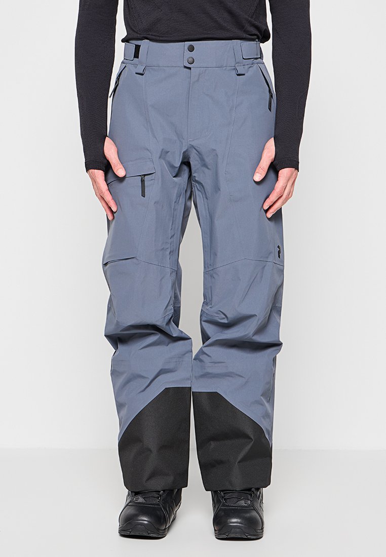 Blaugraue Skihose mit schwarzen verstärkten Unterschenkeln, Reißverschlusstaschen, verstellbarem Bund, getragen mit schwarzen Stiefeln und einem schwarzen Langarmoberteil.