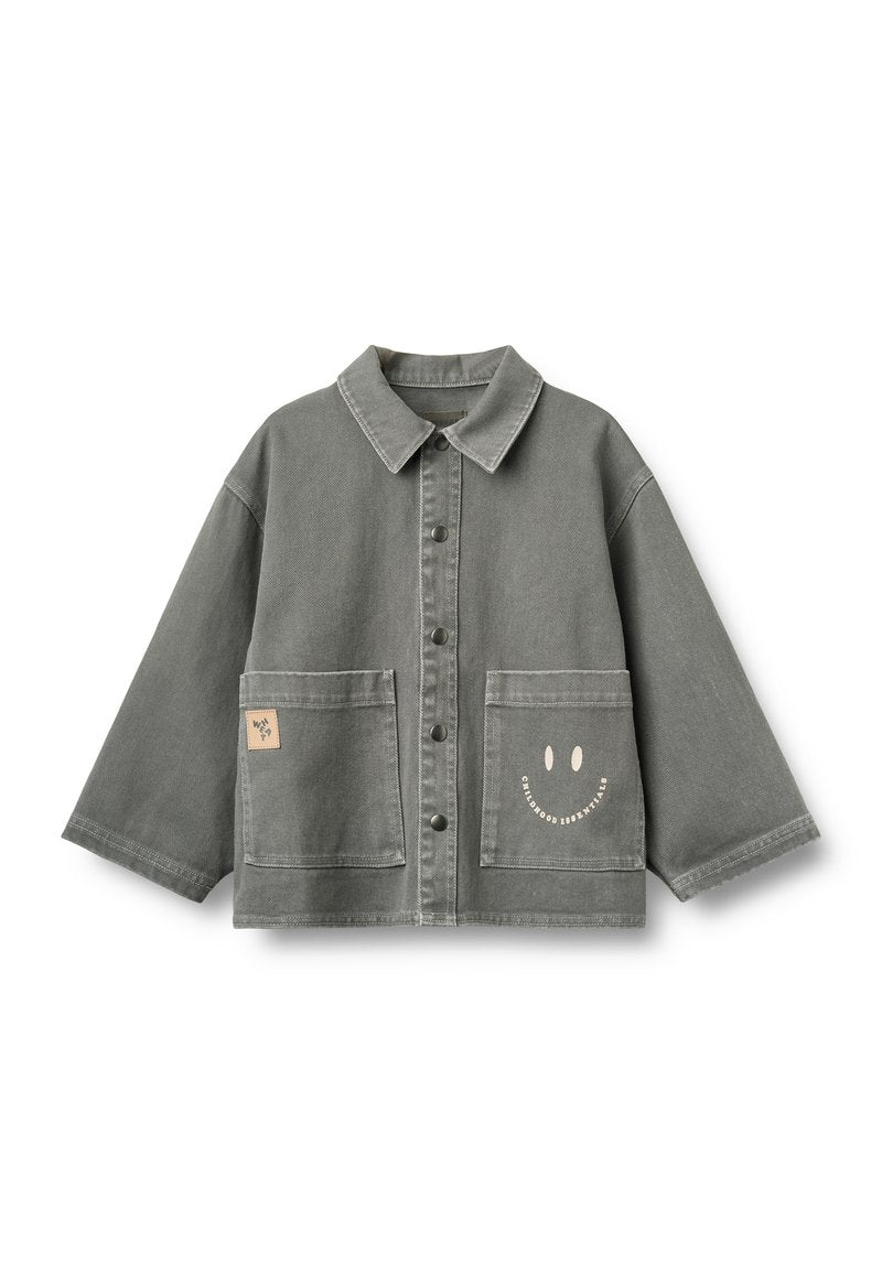 Graue Hemdjacke mit weiten Ärmeln, zwei Fronttaschen, einem kleinen Aufnäher auf der linken Tasche und einem Smiley mit Text auf der rechten Tasche.