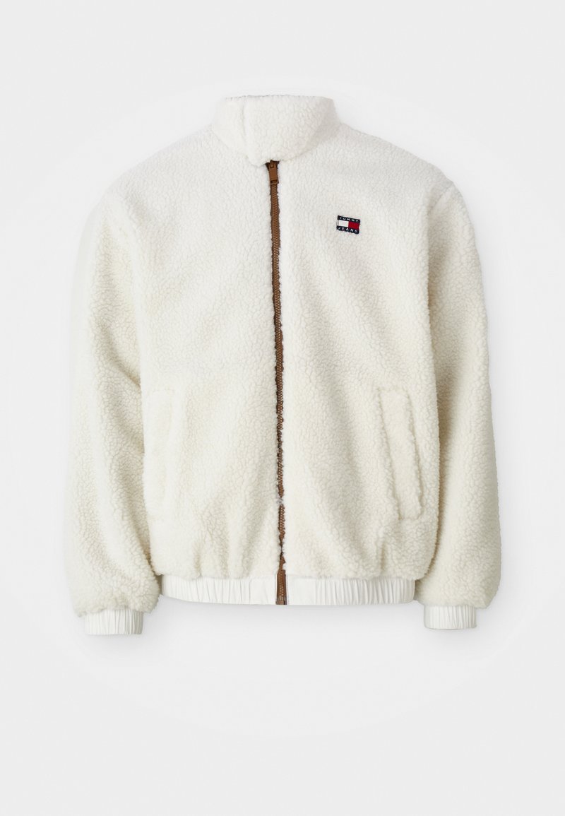 Cremefarbene Fleecejacke mit Stehkragen, zwei Seitentaschen, einem braunen Reißverschluss vorne sowie elastischen Bündchen und Saum. Logo-Patch auf der Brust.