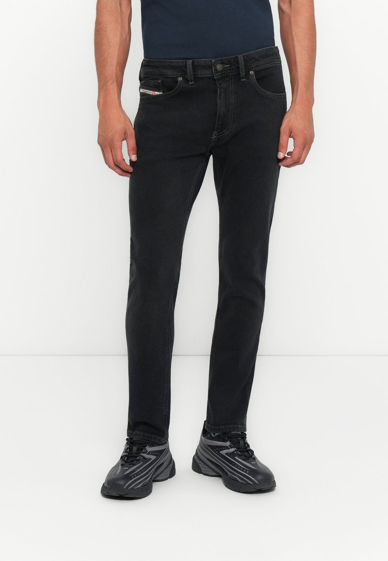 Schwarze Jeans im Slim Fit mit einem Fünf-Taschen-Design und kontrastierenden Nähten. Kombiniert mit schwarzen Sportschuhen.