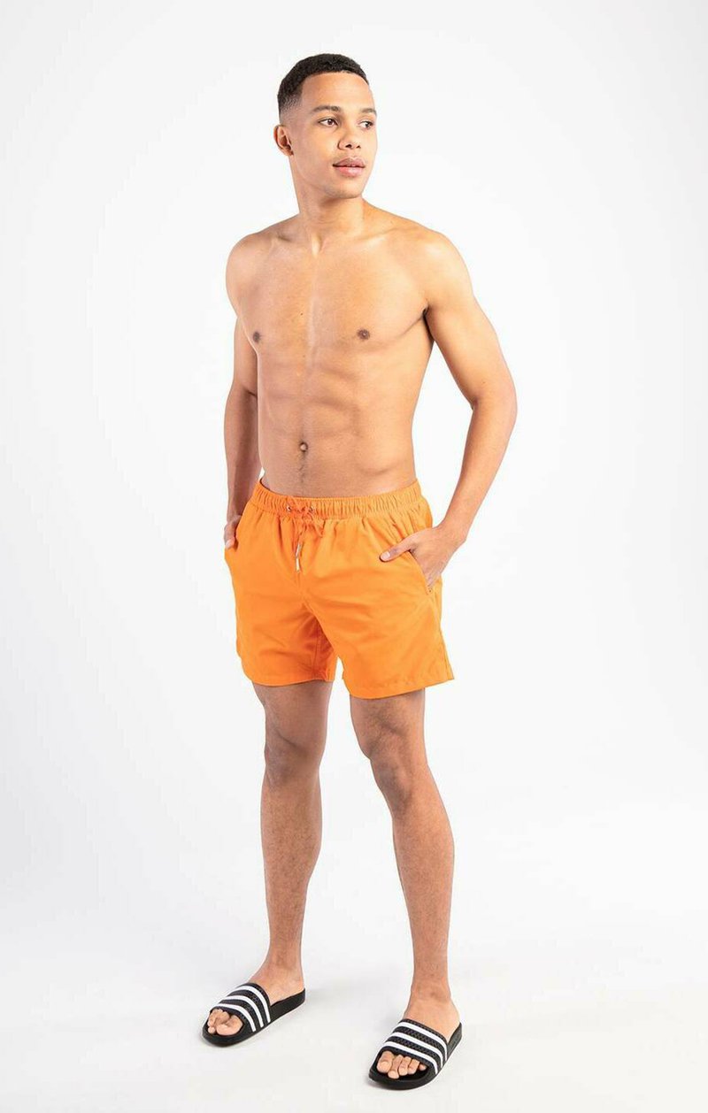 Orangene Badeshorts mit elastischem Bund und Seitentaschen, kombiniert mit schwarz-weißen gestreiften Slides, vor einem schlichten weißen Hintergrund.