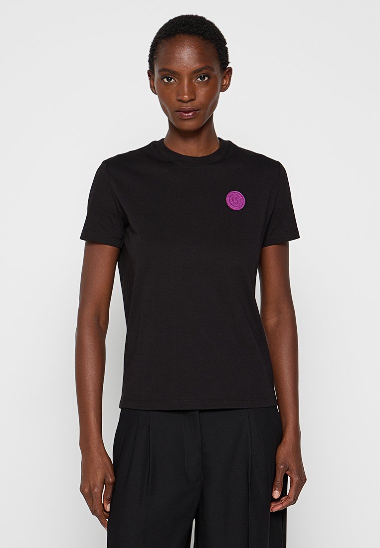 Schwarzes T-Shirt mit kurzen Ärmeln aus Baumwolle, das einen runden Halsausschnitt und ein kreisförmiges lila Logo auf der Vorderseite aufweist.