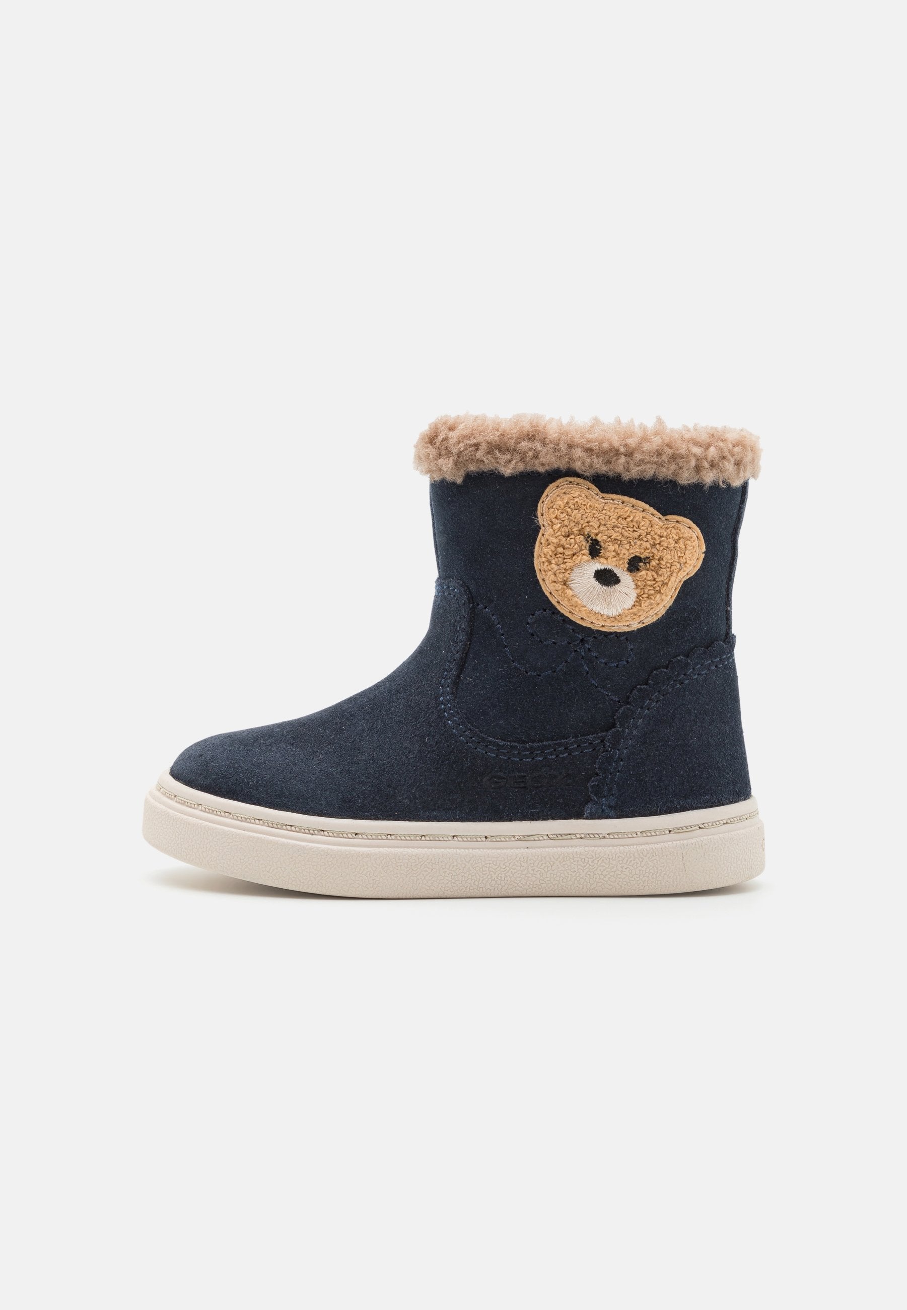 Marineblaue Wildlederstiefel mit einem beigen, flauschigen Schaft, der ein strukturiertes Bärenapplikation an der Seite und eine weiße Sohle aufweist. Kurzes Knöchel-Design.