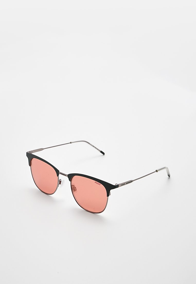 Schwarzmetallic gerahmte Sonnenbrille mit pink getönten Gläsern, mit einer Katzenaugenform und schlanken Bügeln. Auffälliges Branding auf dem Rahmen.