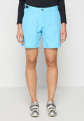 Person in hellblauen Shorts, schwarzem Langarmoberteil und silberweißen Radschuhen steht vor einem weißen Hintergrund.