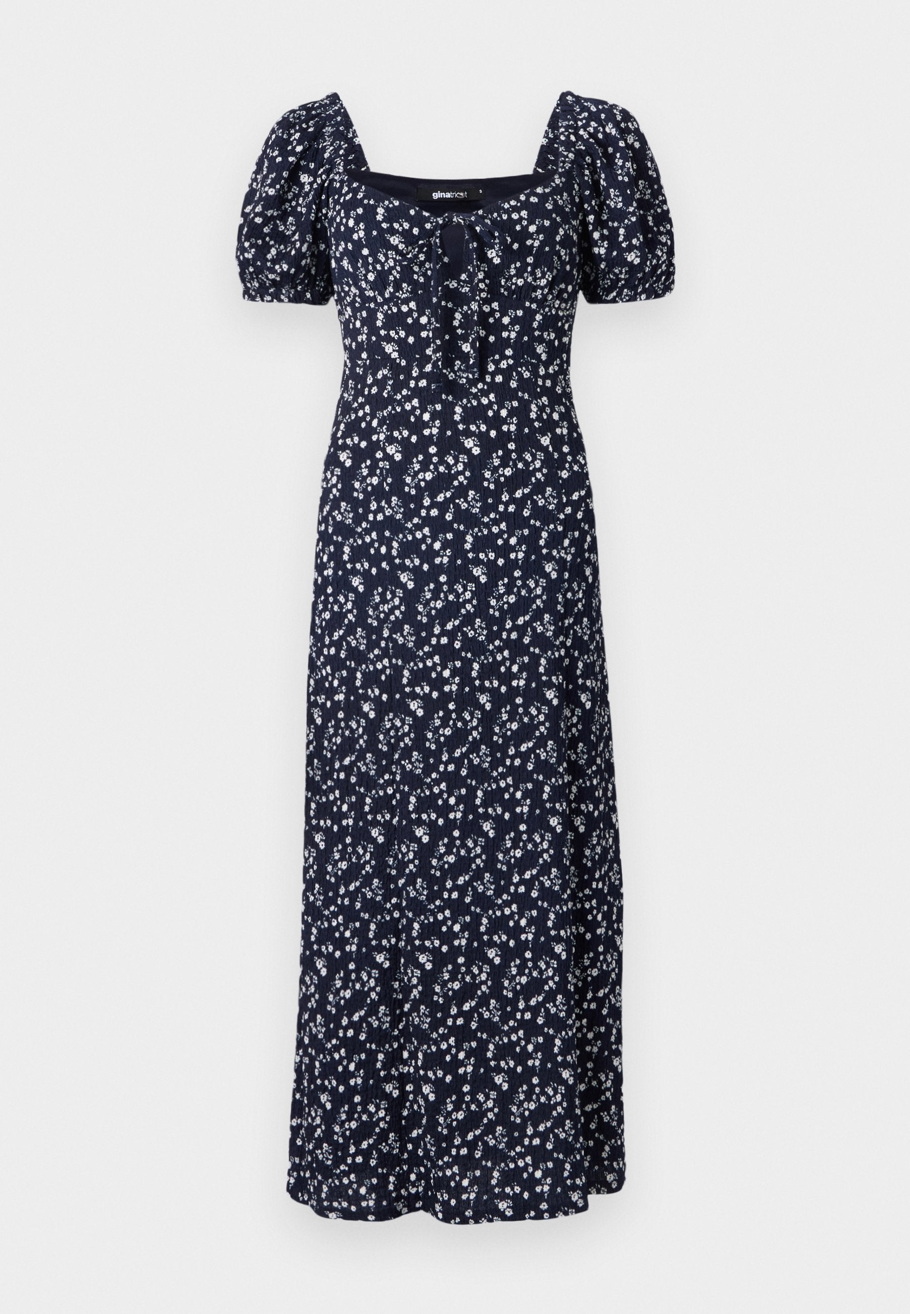 Marineblaues Maxikleid mit Blumenmuster, Puffärmeln, quadratischem Ausschnitt und Bindeband vorne. Das Kleid weist ein verstreutes Muster aus weißen Blumen auf.