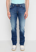 Mann trägt blaue ausgebleichte Slim-Fit-Jeans und weiße Turnschuhe, steht vor einem schlichten hellen Hintergrund.
