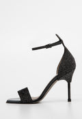 Schwarze High-Heel-Sandale mit glitzernden Riemen, Knöchelriemen und einem einzigartigen, spiralförmigen Stiletto-Absatz auf weißem Hintergrund.