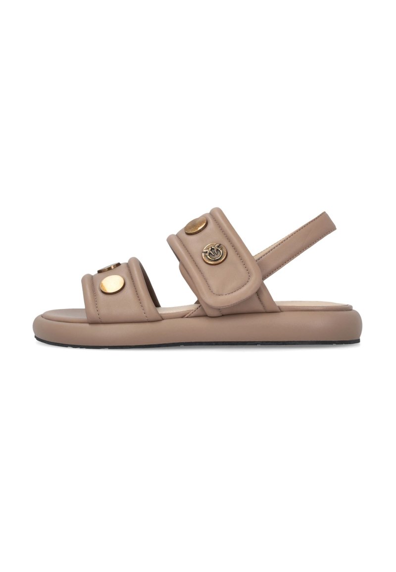 Beige flache Sandale mit zwei gepolsterten Riemen mit goldfarbenen Knöpfen und einem Fersenriemen, auf weißem Hintergrund dargestellt.