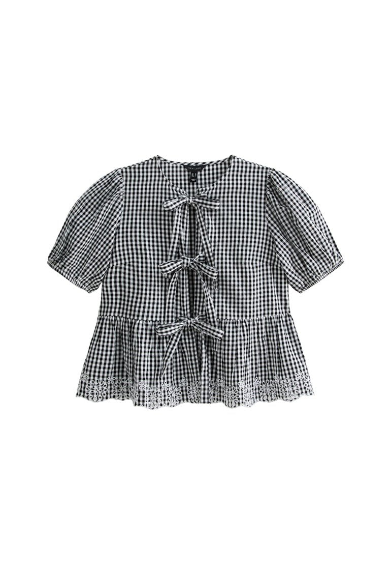 Schwarz-weiße Gingham-Bluse mit kurzen Puffärmeln, drei vorderen Bändern und einer Spitzenborte am Saum. Aus Baumwollstoff, lockere Passform.