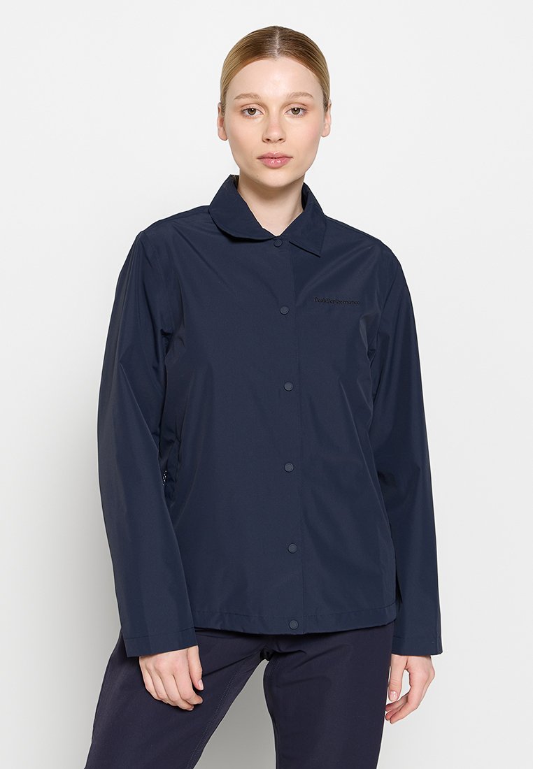 Marineblaue Wasserfesten Jacke mit Kragen, Frontknöpfen und einem Logo auf der linken Brust; glatte Textur und leichtes Design.