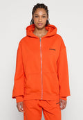Orangenes Zip-Hoodie mit Kängurutasche, entspanntem Schnitt und subtilen schwarzen Logo-Details auf der linken Seite. Weiches Gewebe.