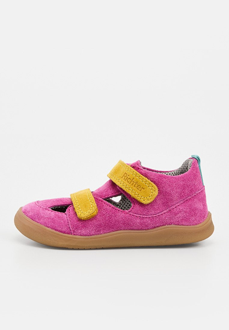 Kinderrosa Wildlederschuh mit zwei gelben Klettverschlüssen und einer braunen Gummisohle, Seitenansicht vor weißem Hintergrund.