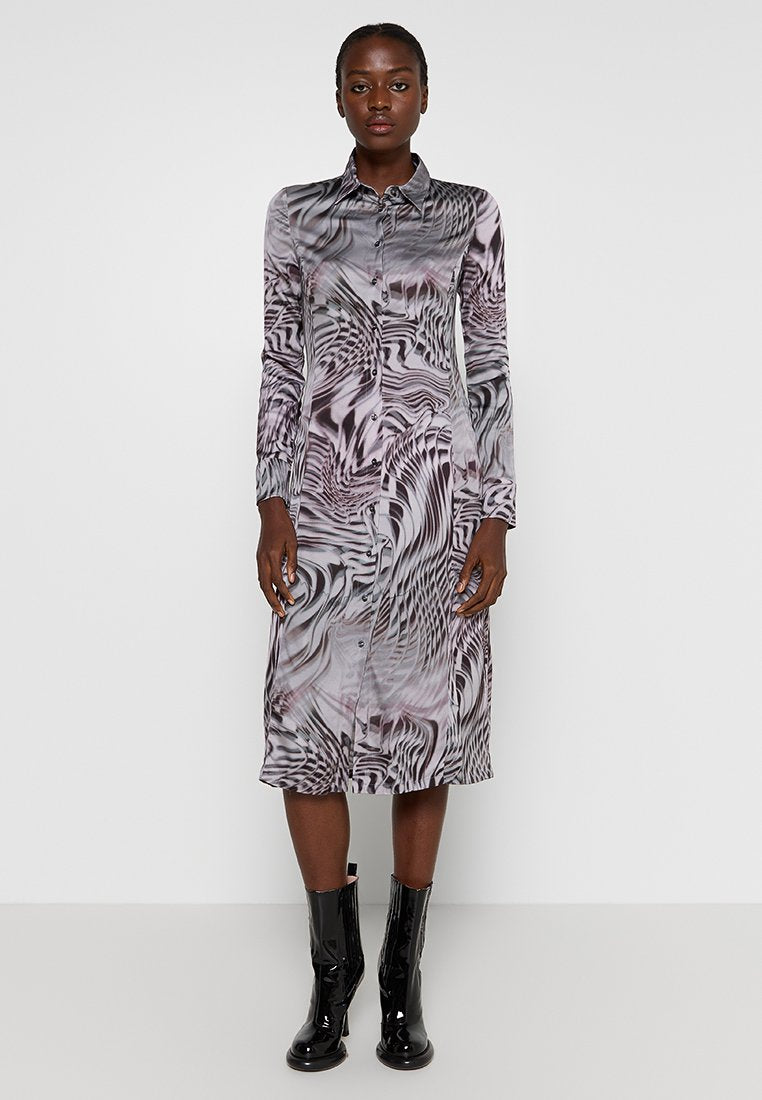 Langärmliges Kleid mit einem fließenden, abstrakten Muster in Schwarz und Grau, mit knöpfbarem Ausschnitt und einem lockeren Schnitt, kombiniert mit glänzenden schwarzen Stiefeln.