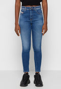 Person, der hochgeschnittene, blaue Skinny Jeans mit Verblendung an den Oberschenkeln und schwarze Sneakers trägt, steht vor einem schlichten weißen Hintergrund.
