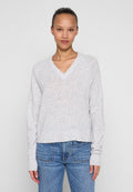 Hellgrauer V-Ausschnittpullover mit langen Ärmeln und gerippten Bündchen, aus einem weichen, strukturierten Stoff. Kombiniert mit blauen Jeans.