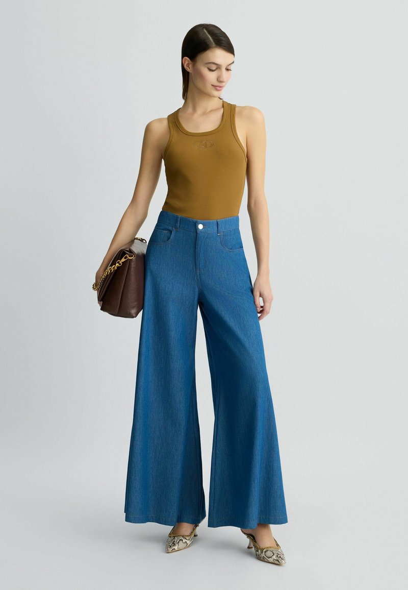 Geripptes senfgelbes Tanktop, hoch taillierte, blaue weit geschnittene Jeanshose und bedruckte spitze Pumps, kombiniert mit einer braunen Schultertasche.