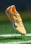 Nike-Fußballschuh mit gelbem Obermaterial, blauen Akzenten und strukturiertem Design. Verfügt über einen orangefarbenen Farbverlauf, sechs blaue Stollen und ein Schnürsystem.