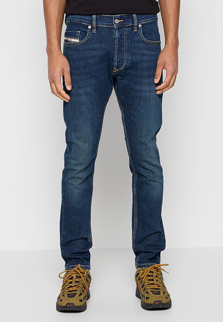 Dunkelblaue Jeans aus Denim. Eng anliegendes Design mit klassischem Fünf-Taschen-Layout und kontrastierenden gelben Nähten. Kombiniert mit braunen Schuhen.