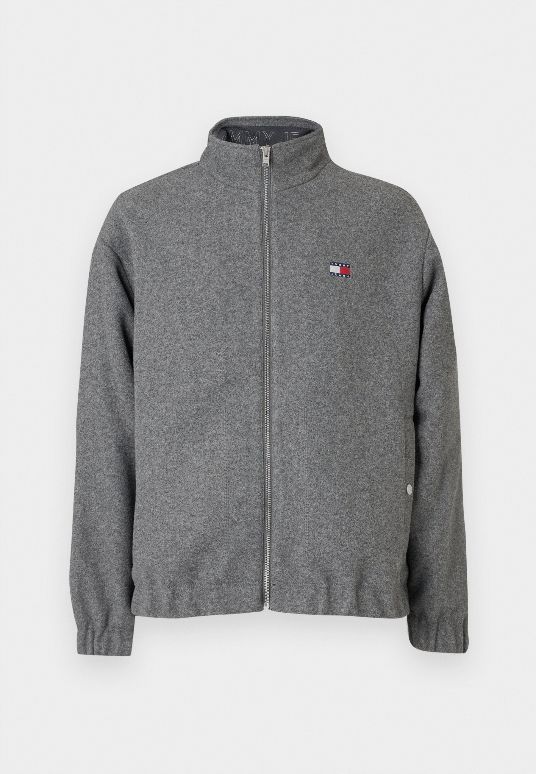 Graue Zip-Jacke aus weichem Stoff, mit hohem Kragen, elastischen Bündchen und einem kleinen Logo-Patch auf der Brust.