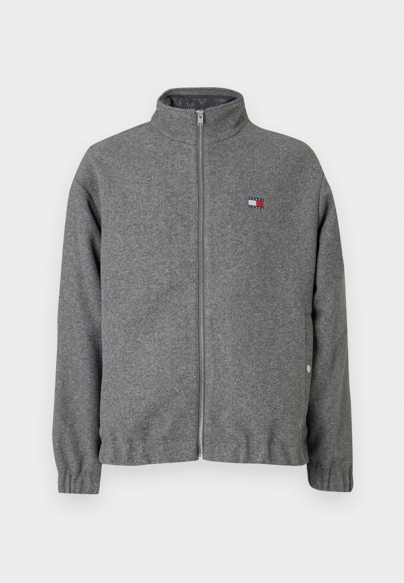 Graue Zip-Jacke aus weichem Stoff, mit hohem Kragen, elastischen Bündchen und einem kleinen Logo-Patch auf der Brust.
