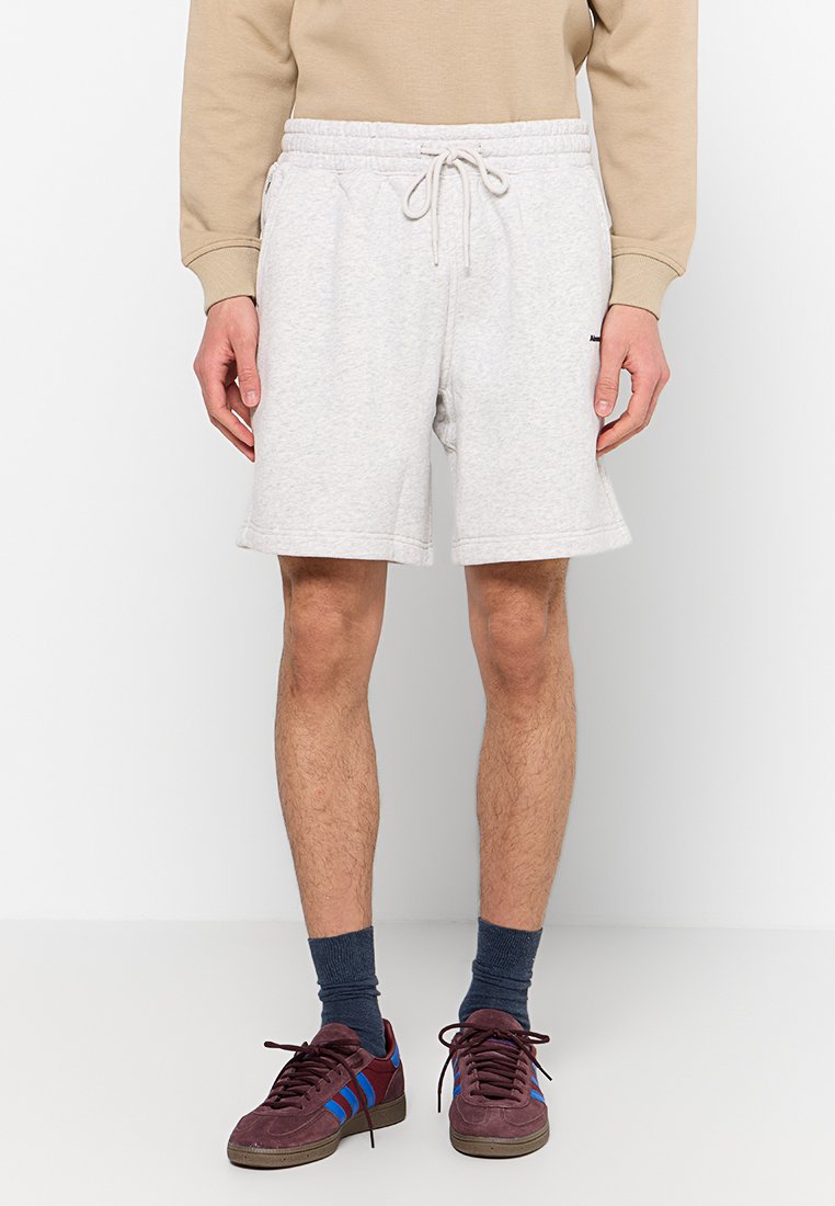 Graue Baumwoll-Sweatshorts mit elastischem Bund und Kordelzug. Verfügt über seitliche Taschen und eine lässige Passform, kombiniert mit bordeauxfarbenen Sneakers.