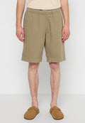 Beige Baumwollshorts mit elastischem Taillenbund, knielang, mit seitlichen Taschen und einem sauberen Saum. Kombiniert mit braunen Schlupfschuhen.