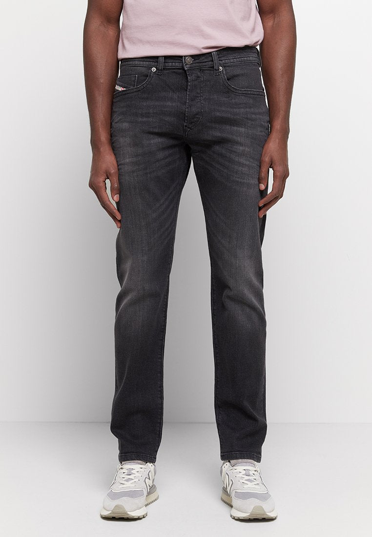 Schwarze Denim-Jeans mit geradem Bein, leichter Ausbleichung, fünf Taschen und einem kleinen Logopatch hinten. Kombiniert mit grauen Sneakers.