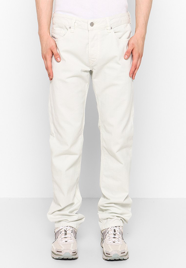 Hellbeige Chinos mit geradem Schnitt, ausgestattet mit Taschen vorne, Knopfverschluss und Nähdetails. Kombiniert mit leichten Sportschuhen.