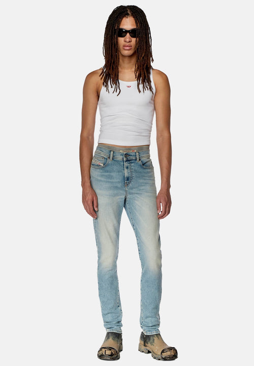 Hellblaue Denim-Jeans mit leichter Abnutzung, kombiniert mit einem eng anliegenden weißen Tanktop und schwarzen Sonnenbrillen. Klobige, gemusterte Schuhe runden den Look ab.