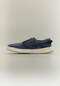 Legerer marineblauer Sneaker mit weißer Sohle, niedrigem Schnitt, Schnürverschluss vorne und Stofflasche an der Ferse vor neutralem Hintergrund.