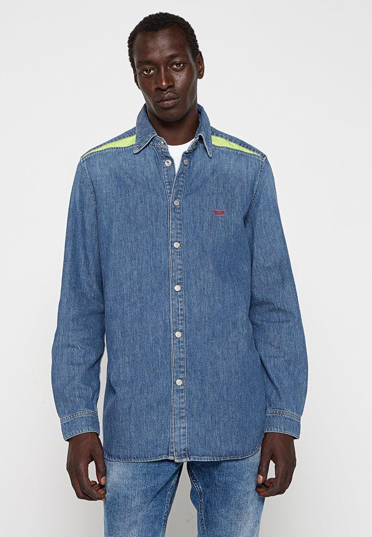 Blaue Jeanshemd mit spitzem Kragen, kontrastierenden grünen Akzenten an den Schultern, knöpfbare Front und ein kleines rotes Logo auf der Brust.