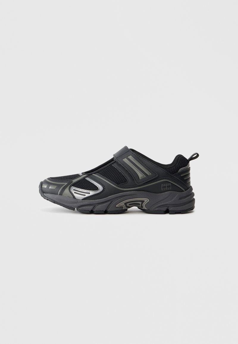 Schwarze Sportschuhe mit einem Netzobermaterial, Gummisohle und silbernen Akzenten. Verfügt über ein Slip-On-Design mit einem Klettverschlussriemen für einen sicheren Sitz.
