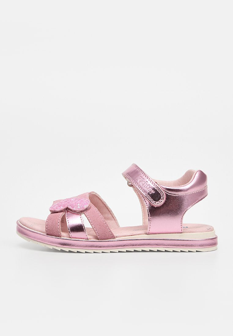 Metallisch pinke Kindersandale mit verstellbaren Klettverschlüssen, glitzerndem Herzdetail vorne, gepolsterter Sohle und strukturierter weißer Außensohle.