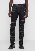 Mann trägt schwarze Acid-Wash-Jeans mit dem Text "PEGAD" auf dem Oberschenkel und schwarze Sneakers, steht vor einem schlichten weißen Hintergrund.