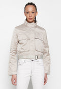 Beige cropped Jacke mit hohem Kragen, zwei frontalen Taschen und passendem Gürtel-Detail. Glattes, leichtes Material mit subtiler Schattierung.